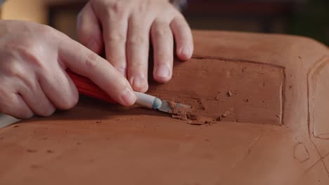 close up of man automotive designer's hands using rake or wire to create details in the sculpture of car clay in the studio