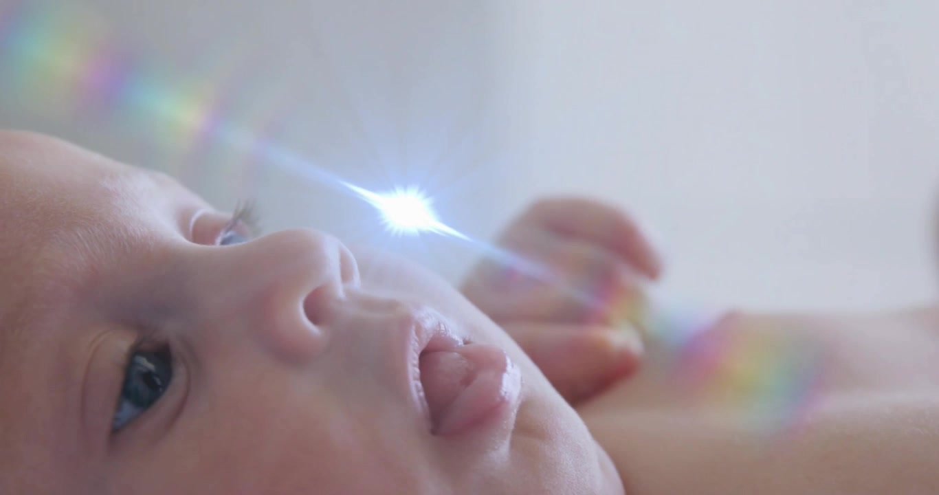 仰向けに寝た女の赤ちゃんが、通り過ぎる虹色のプリズム光を追い、健康デモのためにまばたきしている。