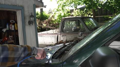 a man blows a pile of leaves off of their car to start repairs