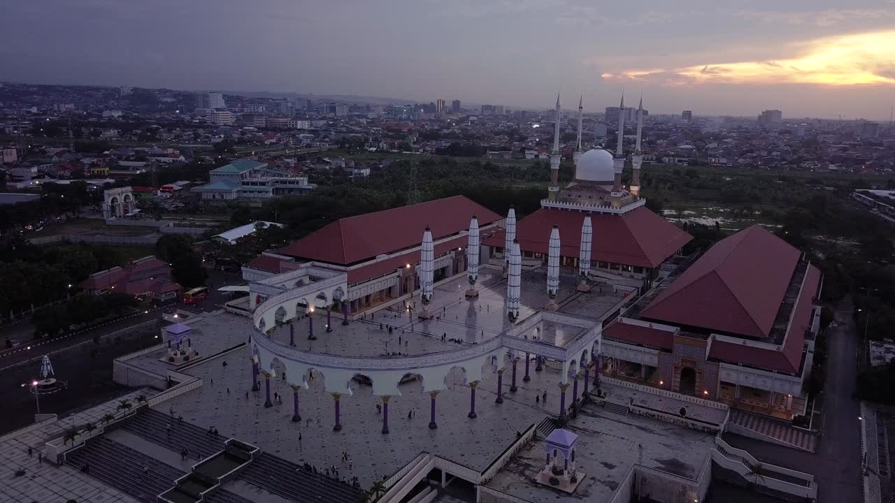Sliding drone shot of the great Mosque of Central Java (MAJT) in suset time. Th sun is orange and the weather is cloudy. It have some pillars and some umbrela that is closed