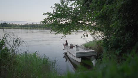 hombre pescando una boa estacionada en el borde del río zambezi que fluye