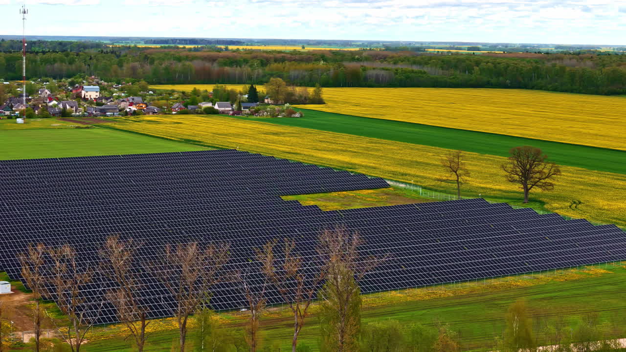 A solar farm with expansive green fields and a village in the background, aerial view