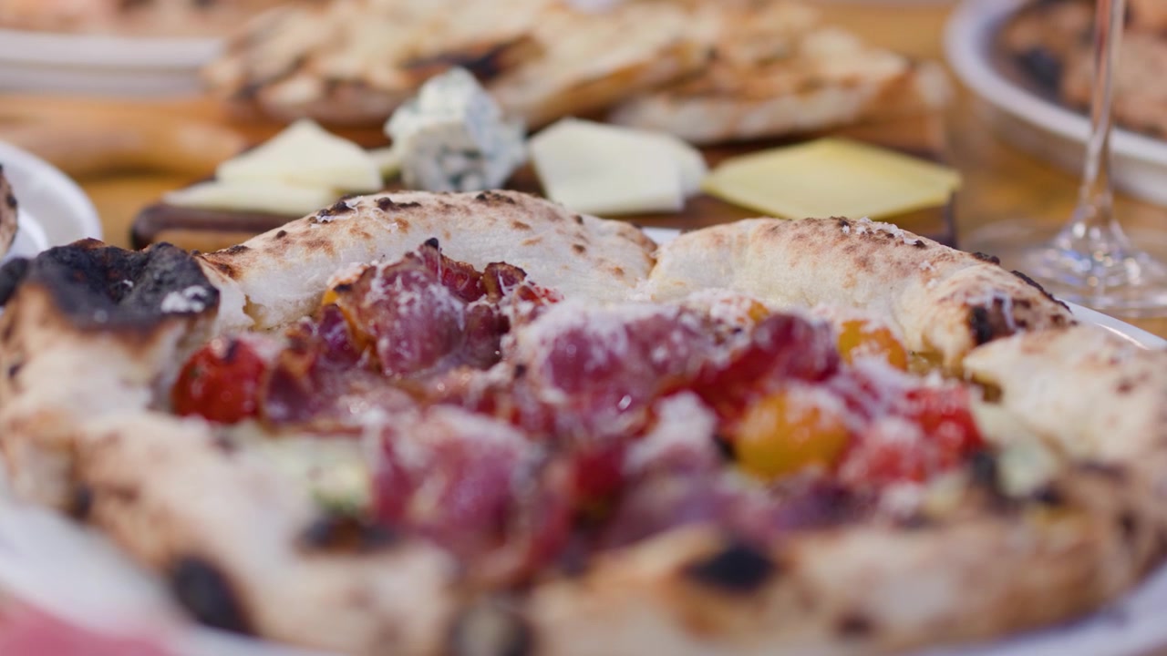 Panoramica ravvicinata di pizze artigianali a lievitazione naturale e tagliere di formaggi con calda illuminazione da ristorante.