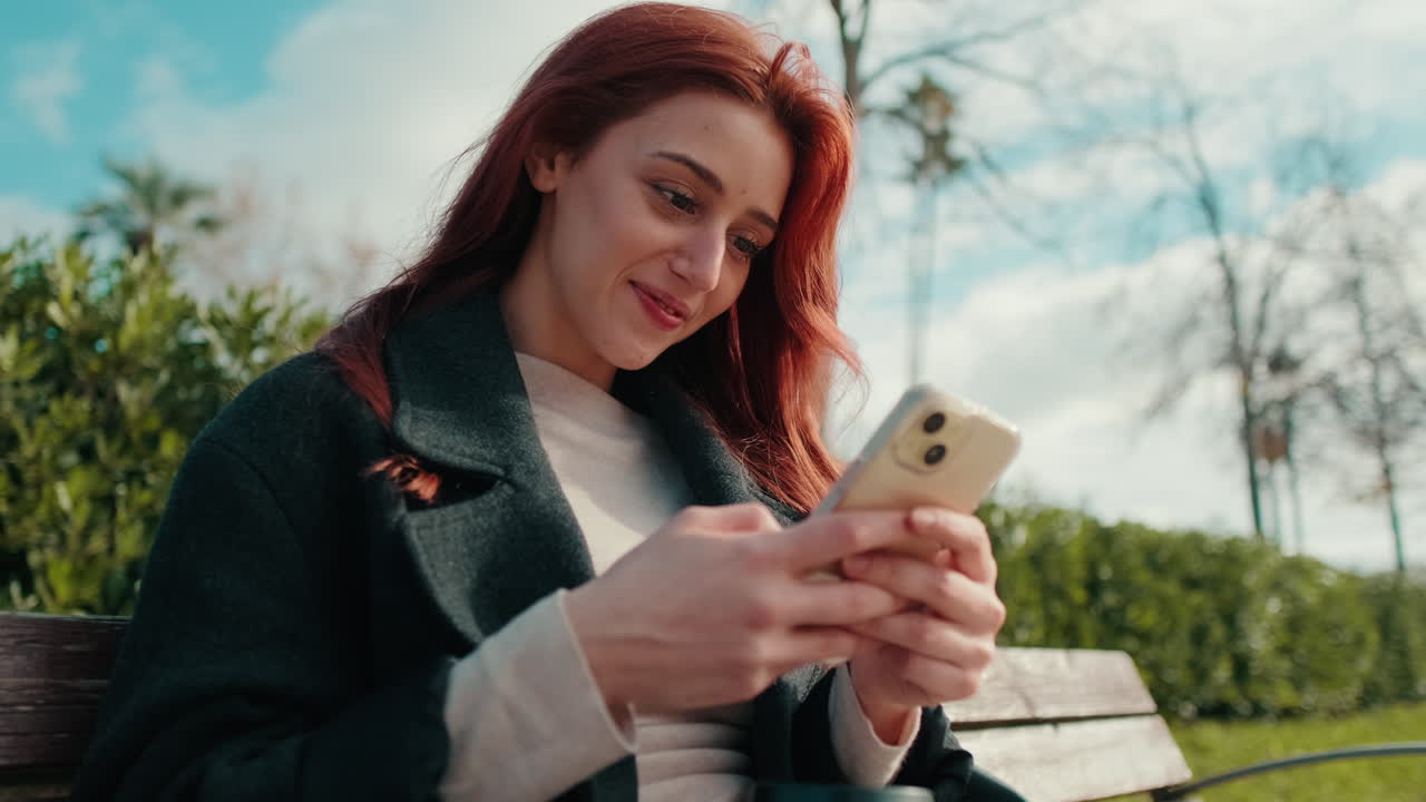 Giovane donna sorridente che usa lo smartphone su una panchina del parco