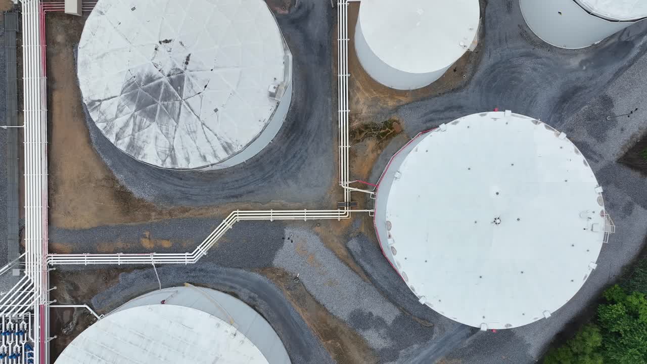 Aerial top down of several white fuel tanks connected with pipelines. Suburb district of America. Town. Petroleum and aviation fuel area