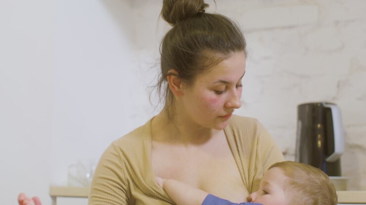 Close Up Of A Young Mother Working With Laptop Computer And Breastfeeding Her Baby Boy At Home