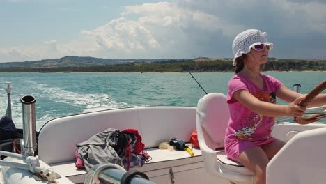 little girl with sunglasses and hat drives motorboat