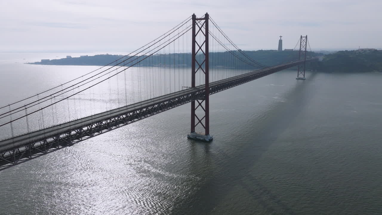 Cinematic aerial drone shot of the red 25th April suspension bridge over the Tagus river in Lisbon, Portugal, with a single car crossing before running event