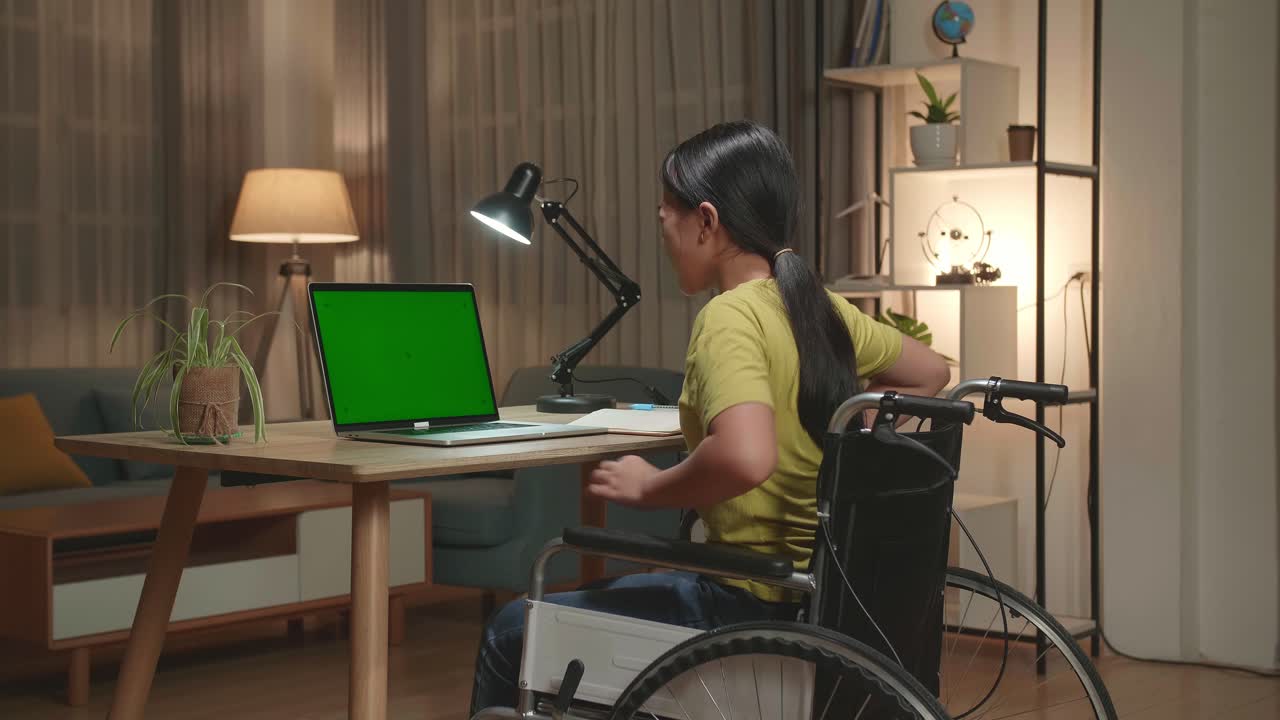 Asian Kid Girl Sitting In A Wheelchair Using Laptop Computer With Mock Up Green Screen And Pain Her Back At Home