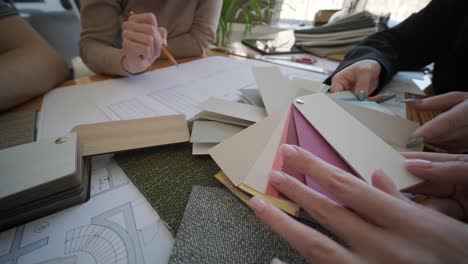 un equipo de diseñadores de interiores colabora en una mesa, examinando planes arquitectónicos, muestras de tela y paletas de colores, planeando un proyecto de diseño