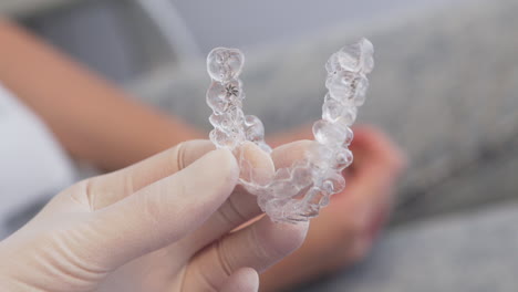 primer plano apretado de una mano enguantada sosteniendo dos alineadores invisalign, con el paciente en el fondo