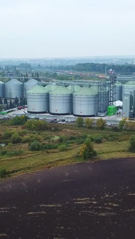 numerous metal elevator tanks at the territory of modern granary plant. drone shot distancing from a huge industrial area locating in the fields. vertical video