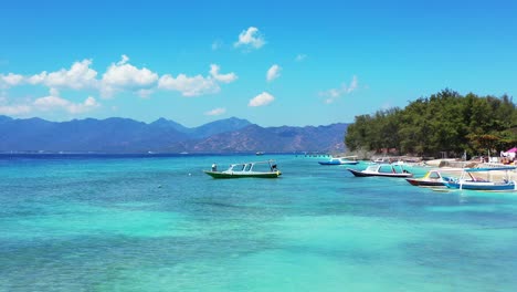 Boats-anchoring-on-shore-of-tropical-island-with-white-sandy-beach-washed-by-calm-clear-water-of-blue-turquoise-lagoon-on-a-bright-sky-in-Bali