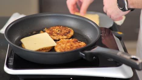 close-up of adding cheese to chicken burgers while frying on a hotplate