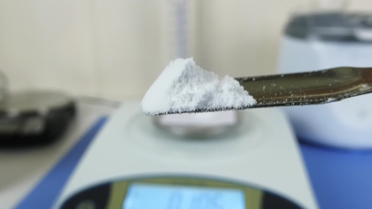 Close-up of a laboratory technician's gloved hands performing a quality control test on hyaluronic acid powder in a cosmetic laboratory.