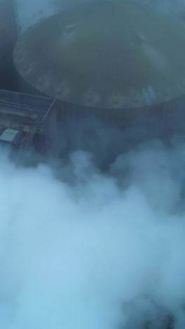 huge functioning agribusiness plant for grain storage and processing. top view on the silo tanks roofs in the white smoke and fog. vertical video