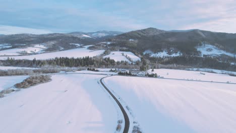 Drohne-Fliegt-über-Eine-Schmale,-Kurvenreiche-Straße-Inmitten-Einer-Schneebedeckten-Weißen-Berglandschaft