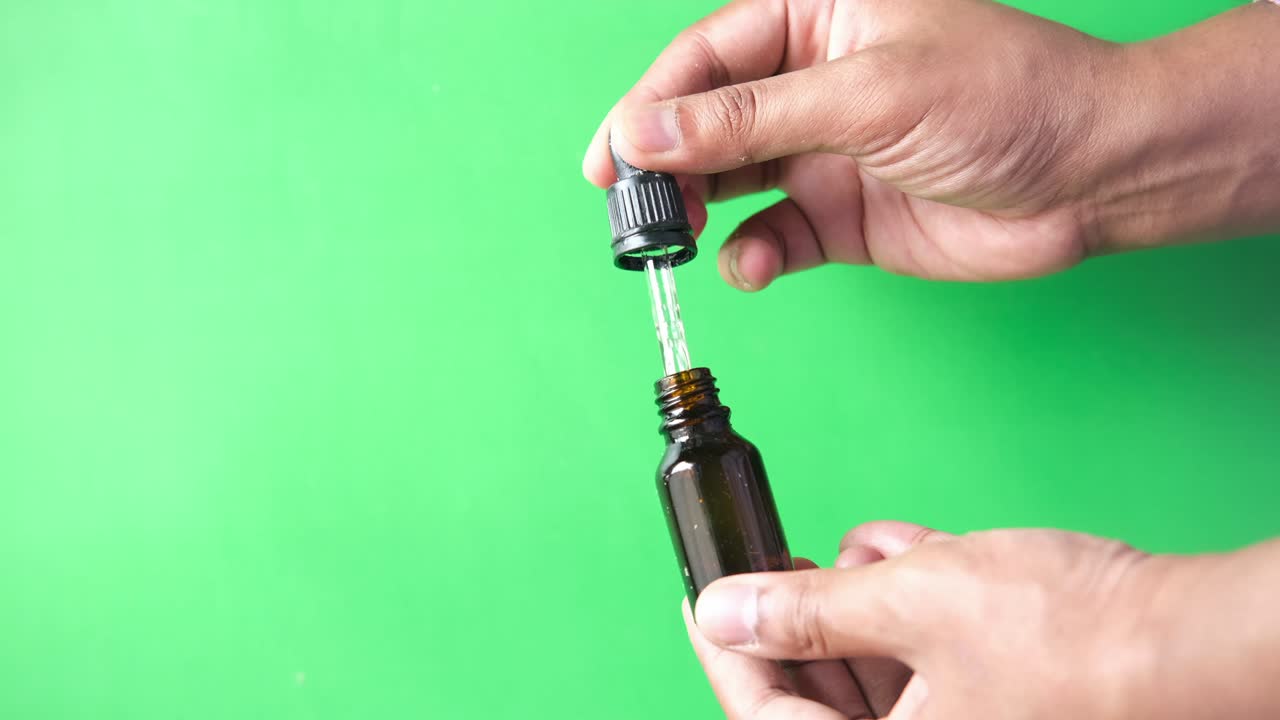 Drop falls from a pipette into a cosmetic bottle against green background