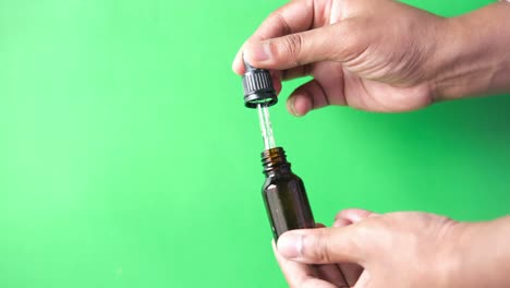 drop falls from a pipette into a cosmetic bottle against green background