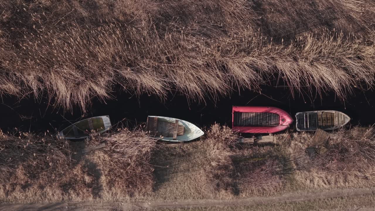 Bovenaanzicht vanuit de lucht van kleine houten boten afgemeerd langs een smal kanaal omringd door droog riet