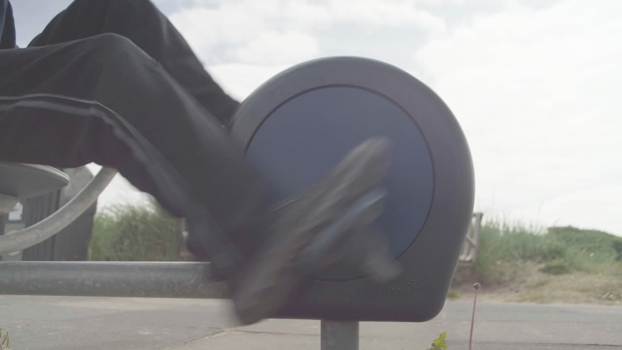 An adult&rsquo;s legs and feet exercising on an exercise bike at the beach