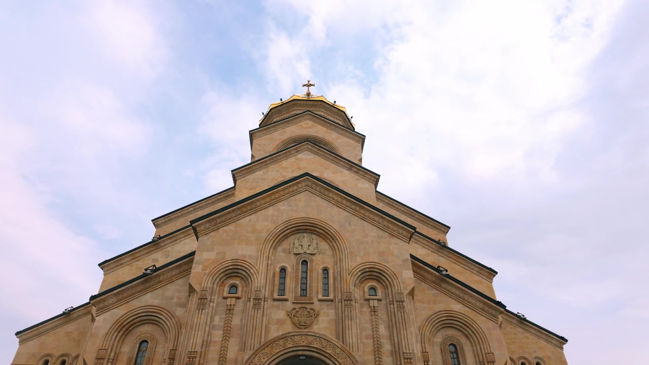 Vista dal basso dell'imponente cupola dorata e delle sezioni superiori della Cattedrale della Santissima Trinità a Tbilisi, Georgia. L'ornata struttura religiosa si erge maestosa contro un cielo parzialmente nuvoloso, mettendola in mostra.