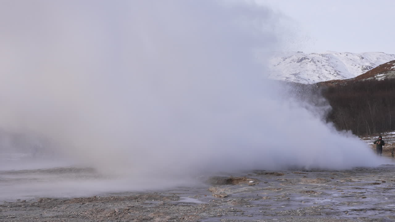 turista viendo strokkur geysir en islandia durante el invierno
