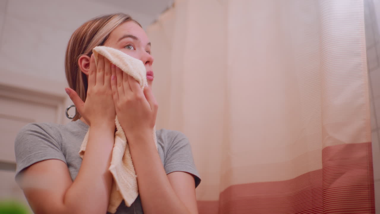 Young woman covers face with towel to dry after washing in bathroom, focusing on skincare and hygiene routine, natural skin with acne, beauty care, refreshing daily ritual