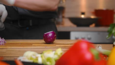 Frische-Rote-Zwiebel,-Die-Von-Einem-Jungen-Professionellen-Männlichen-Koch-In-Einem-Eleganten-Schwarzen-Hemd-Mit-Tätowierungen-Auf-Einem-Holzbrett-Geschnitten-Wird