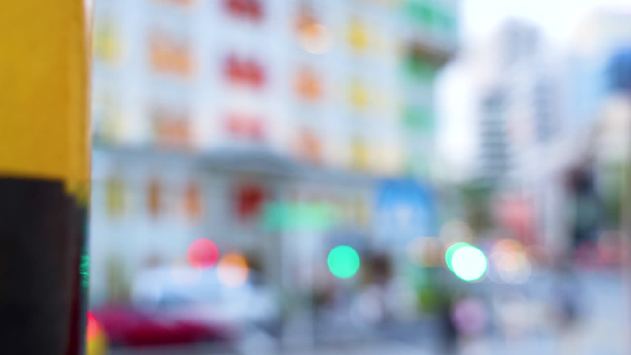 A yellow and black striped pole moves across a defocused city street, with colorful buildings, vehicles, and traffic lights in bright daylight