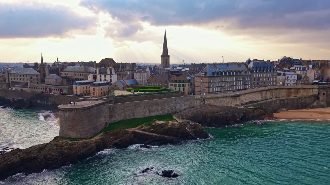 Saint Malo Intra Muros i Ille-et-Vilaine, Bretagne, Frankrig, med befæstede granitvægge, der rejser sig fra den klippefyldte kystlinje mod Saint Vincent-katedralens spir over horisonten, droneoptagelse, der zoomer ind fra havet.