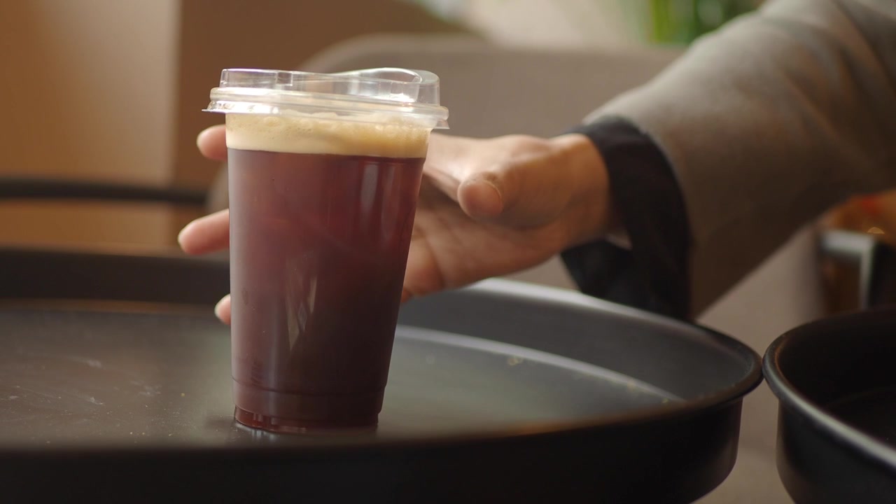 Person Picking Up Iced Coffee from a Tray in a Cafe