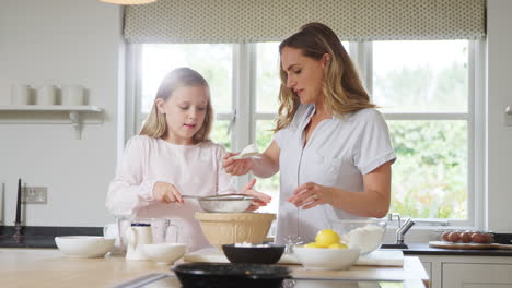 Mother-And-Daughter-Wearing-Pyjamas-Baking-And-Making-Pancakes-In-Kitchen-At-Home-Together