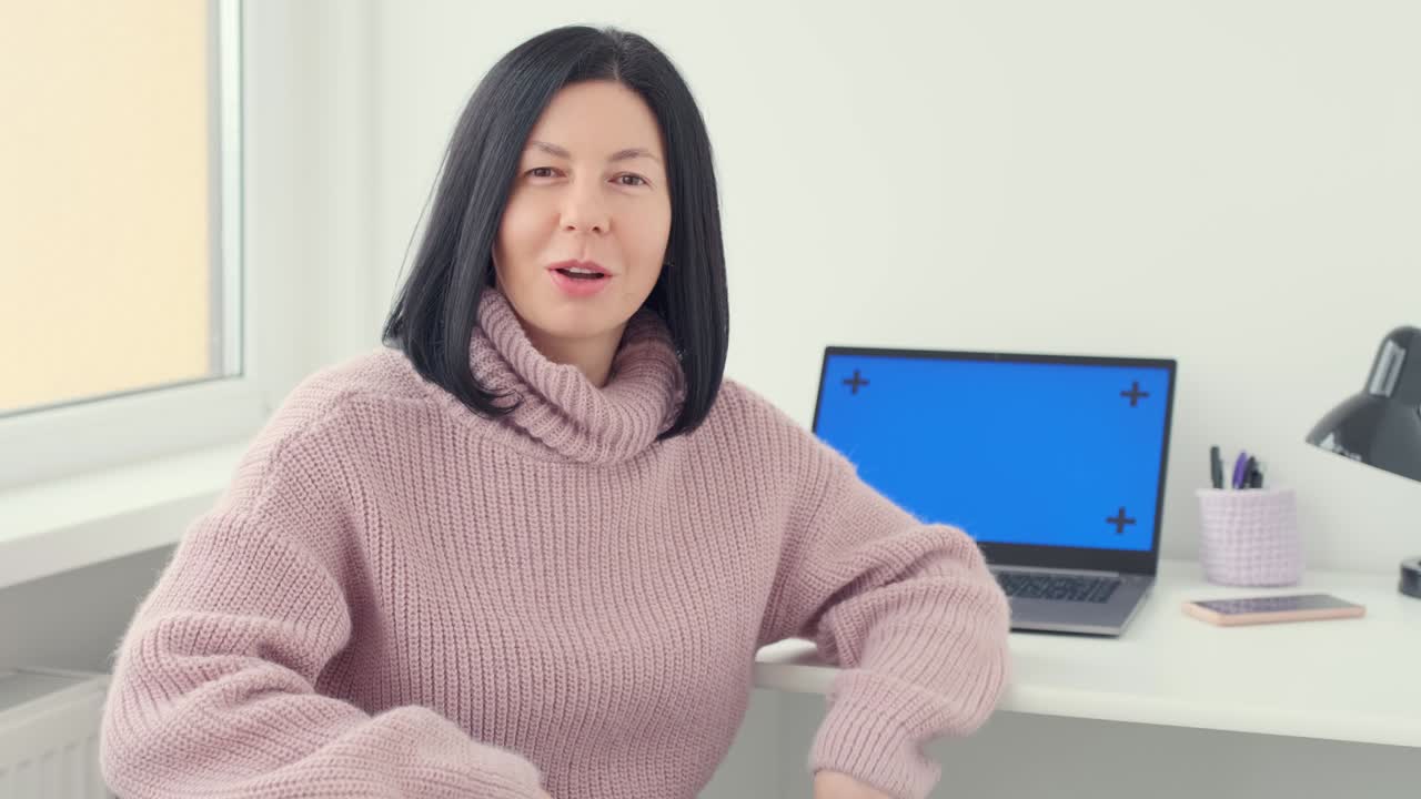 노트북 컴퓨터와 함께 테이블에 앉아있는 여성 여성 vlogger 대표가 말하고, 카메라에 설명하고 집에서 몸짓을합니다.