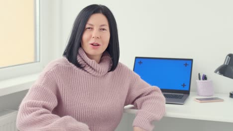 mujer sentada en la mesa con una computadora portátil. representante de vlogger femenina hablando, explicando en la cámara y gestando en el hogar. comercio, negocios.