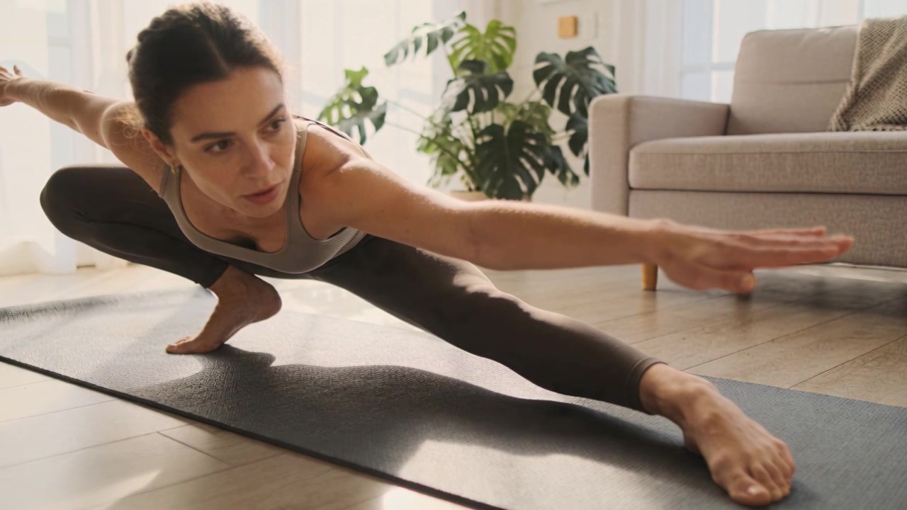 Performing woman in activewear holding low side lunge for balance on yoga mat in living room
