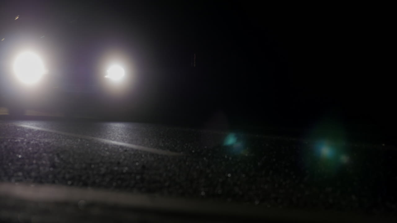 Cars at night filmed from low down on the roadside, headlights passing in a loop