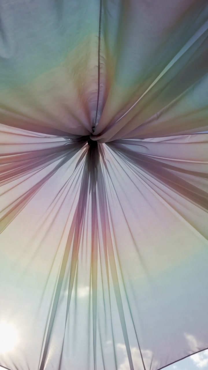 Vertical video: Fluttering sheer fabric canopy from breeze, tightening knot at park, refracting sun