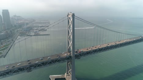 Toma-Aérea-De-Vehículos-Moviéndose-En-El-Puente-De-La-Bahía-De-San-Francisco–oakland-Con-La-Ciudad-Al-Fondo