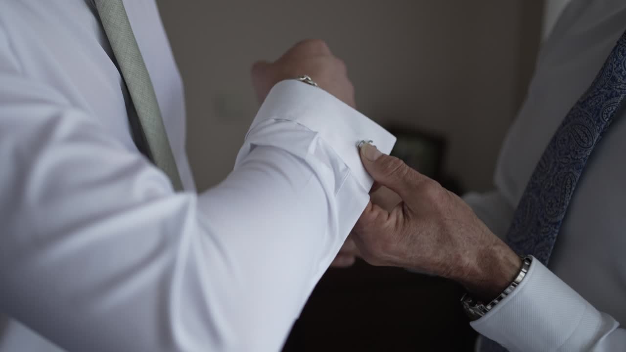 el novio recibiendo ayuda con los gemelos, capturando un momento íntimo de preparación de la boda