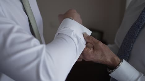 el novio recibiendo ayuda con los gemelos, capturando un momento íntimo de preparación de la boda