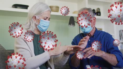 animation of virus cells with senior caucasian couple with face masks disinfecting hands