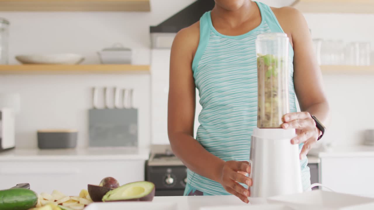 Donna afroamericana felice che prepara una bevanda salutare in cucina.