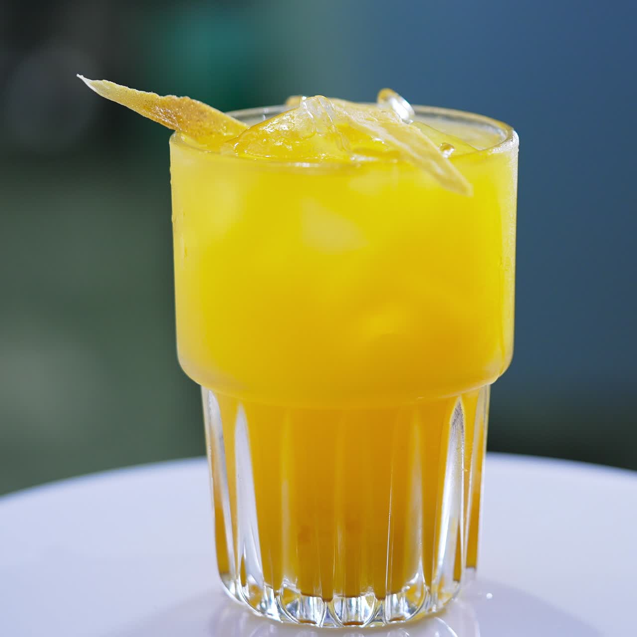 Orange tasty cocktail decorated with ice cubes and chips. Beautiful beverage on the spinning table close up