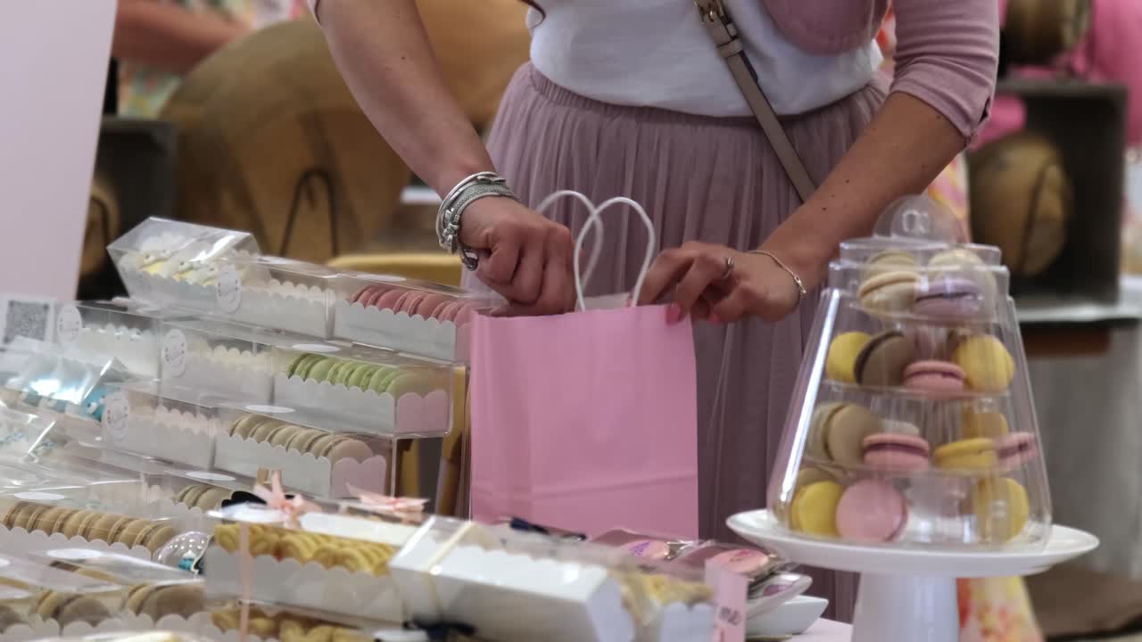 베이커리 시장 에서 고객 을 위해 분홍색 가방 에 매카룬 을 넣고 있는 베이커리 스탠드  에 서 있는 여자