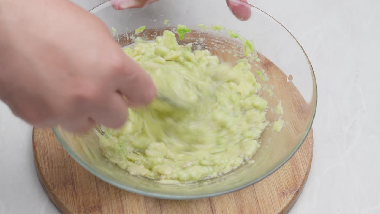 Close-up of avocado mixed with eggs and oil using a fork inside a transparent bowl