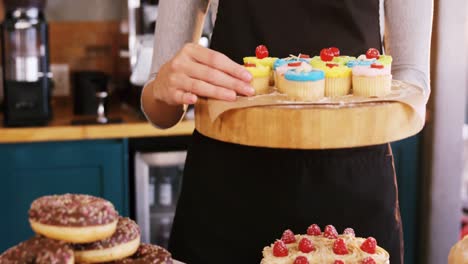 Mid-section-of-waitress-holding-cup-cake-on-tray