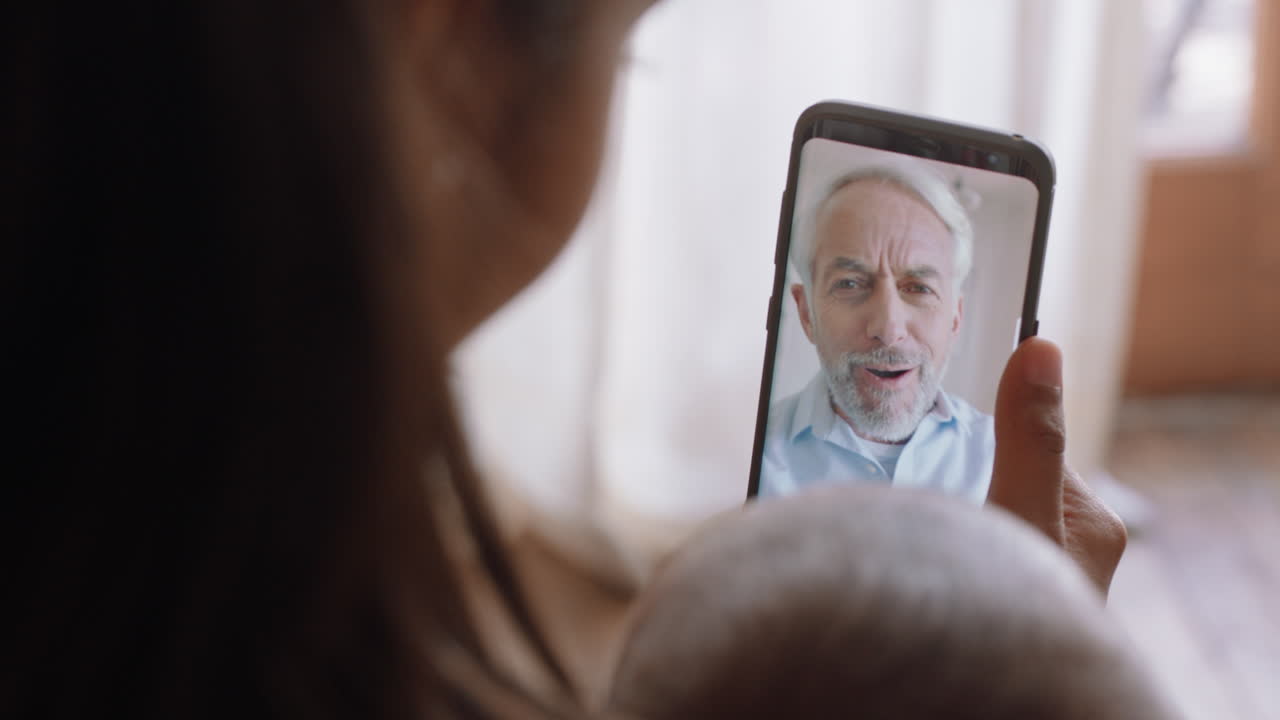 madre joven y bebé chateando por video con el abuelo usando un teléfono inteligente saludando a la nieta disfrutando de la conexión familiar