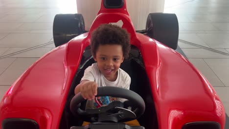 playful 3-year-old kid enjoying in a red f1 toy car inside a mall