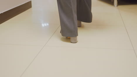 close-up of businesswoman's feet walking in gray heels on office floor with geometric tile pattern, confident professional stride, modern office corridor, stylish and formal footwear